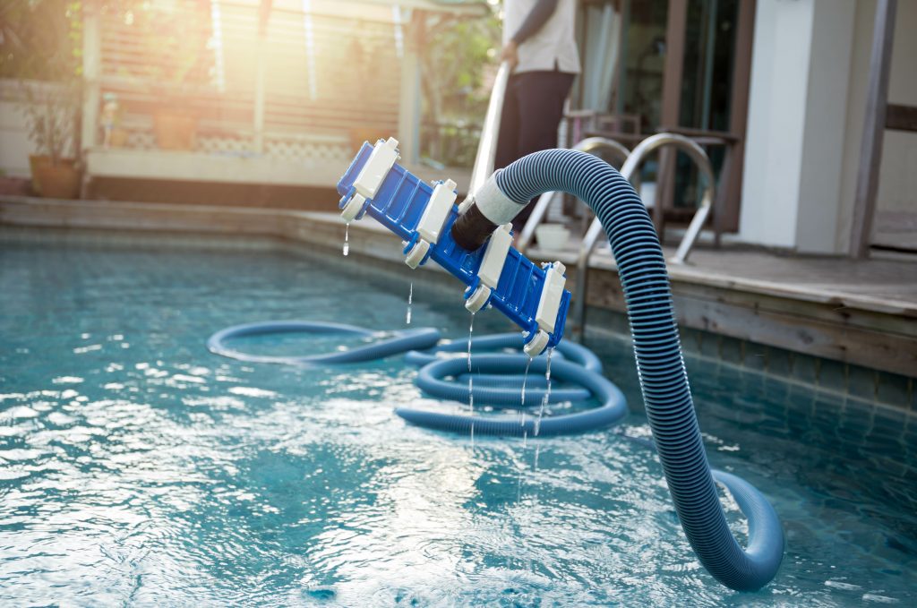 Man cleaning swimming pool with vacuum tube cleaner